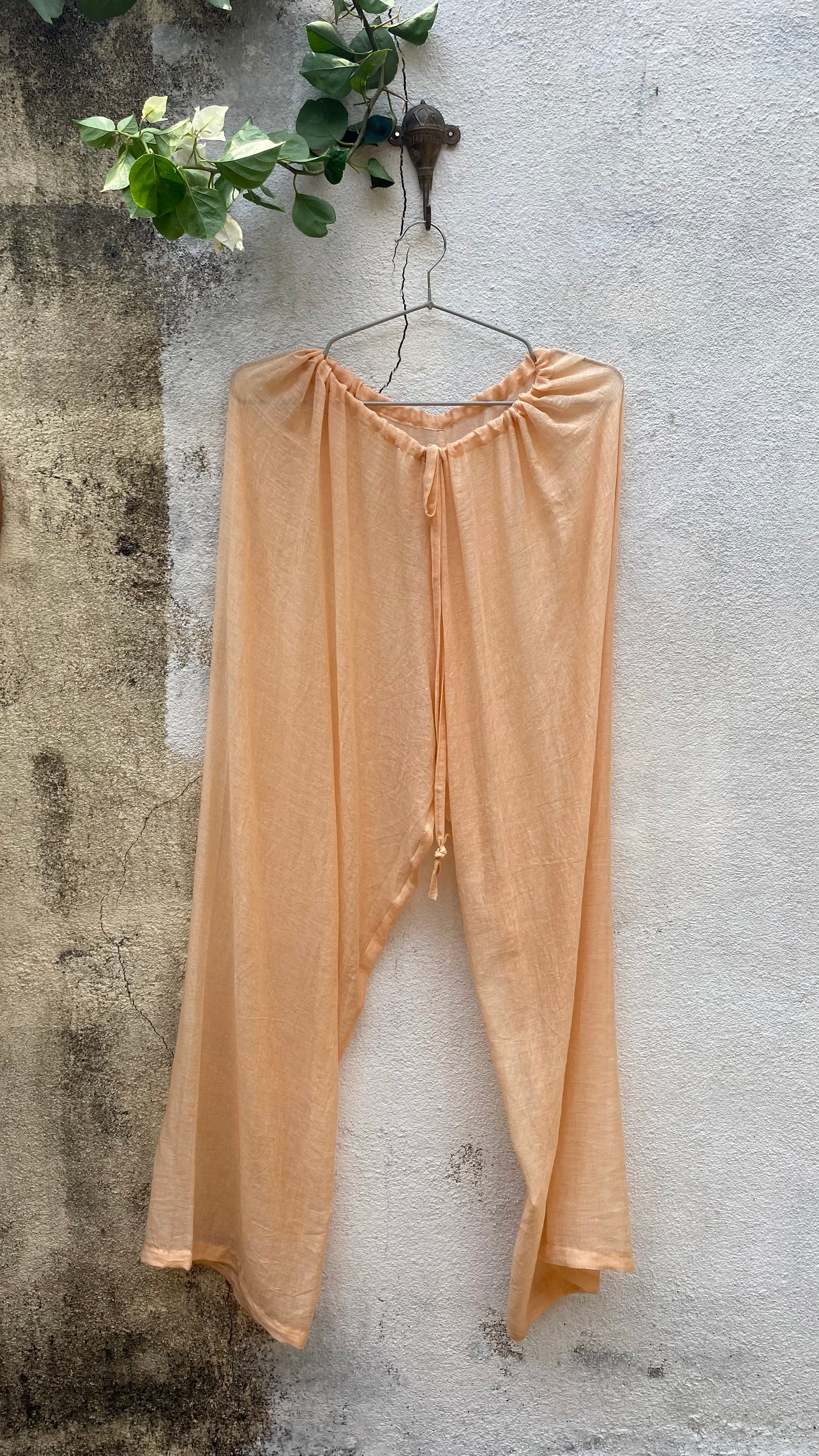 Beige pants hanging on a hook against a textured wall.